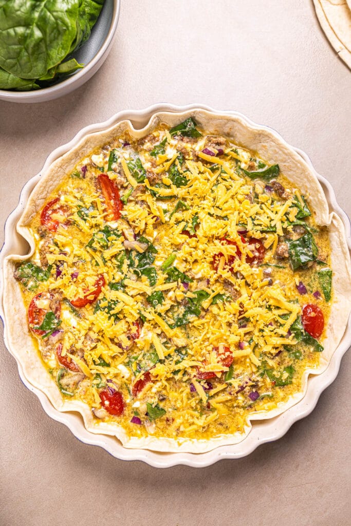 This is an image of tortilla quiche topped with cheese before baking