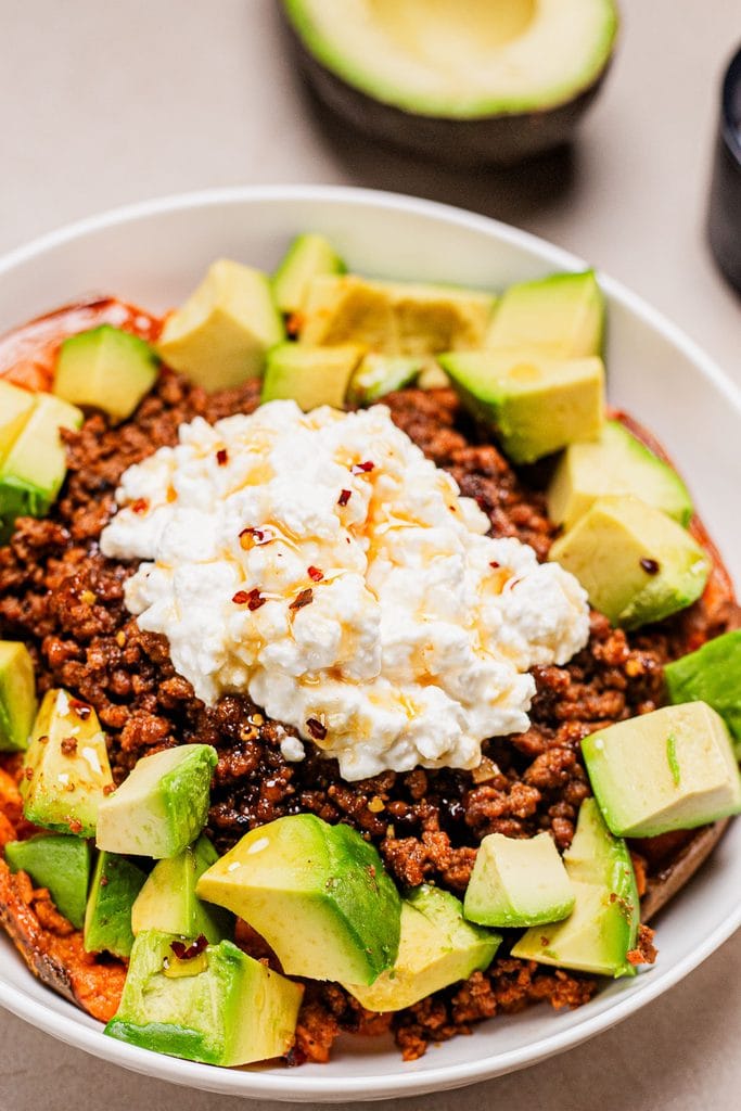 A close up of the loaded baked sweet potato topped with ground beef , cottage cheese and avocado with hot honey.