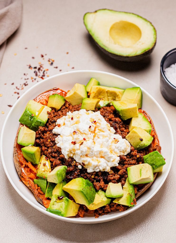 This is an image of a loaded baked sweet potato with ground beef and cottage cheese in a white plate.