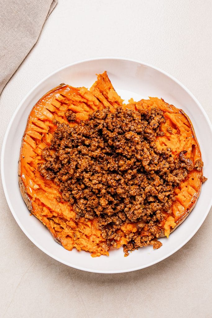 Baked halved sweet potatoes in a white plate topped with saucy ground beef.