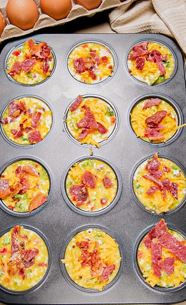 Eggs muffin mixture topped with cheddar cheese and bacon before baking.
