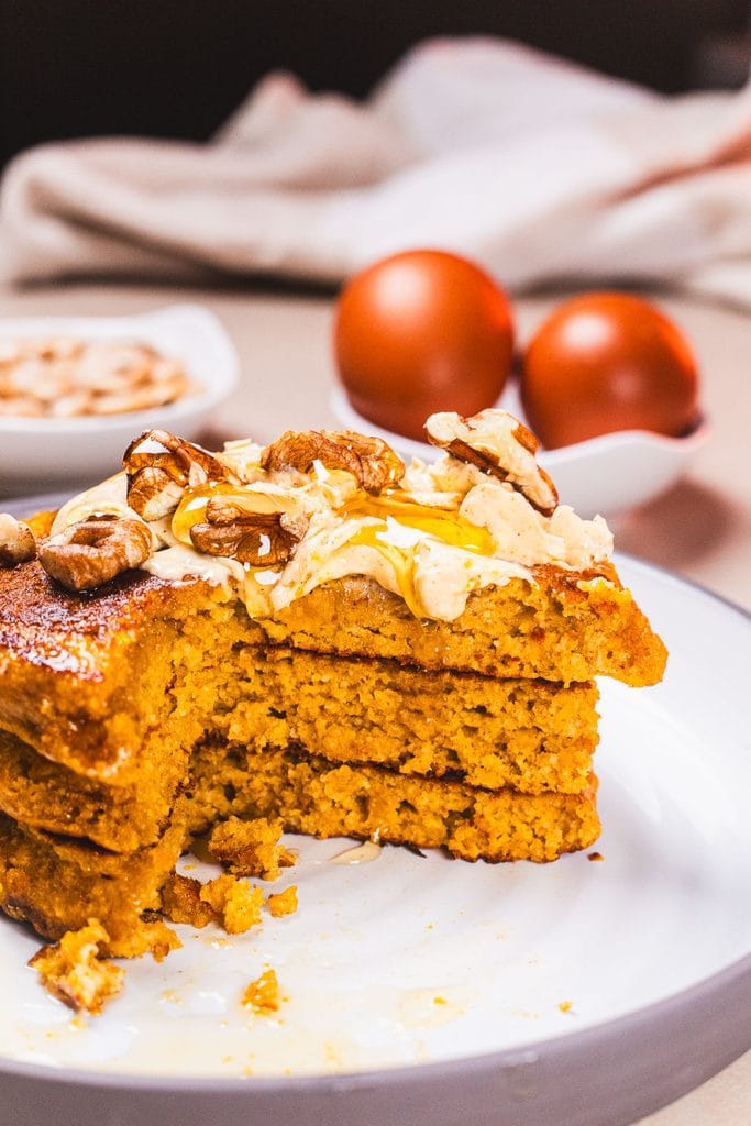 Stack of high protein pumpkin pancakes topped with spiced butter, syrup and pecan nuts.